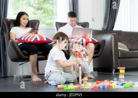Asiatische Bruder und Tochter spielen Holz Spielzeug im Wohnzimmer mit Vater und Mutter im Hintergrund. Glückliche Familie. Stockfoto