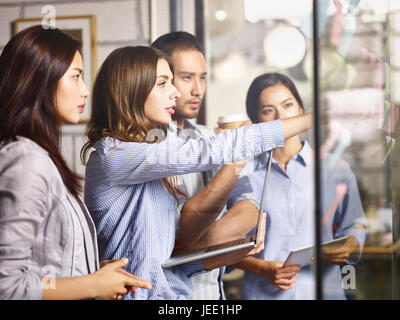 ein Team von kaukasischen und asiatischen Geschäftsleute, die in einer Brainstorming-Sitzung mit Laptop-Computer, digital-Tablette und Post-It Zettel. Stockfoto