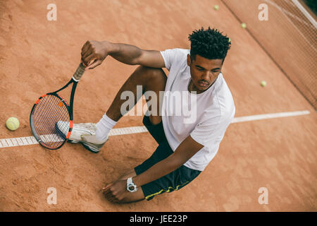 Tennisspieler, die nach dem Tennisspiel auf Boden saßen erschöpft Stockfoto