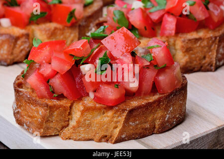 Bruschetta mit Tomaten und Knoblauch auf Holzbrett Closeup schneiden Stockfoto