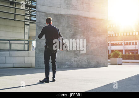 Rückansicht eines Geschäftsmannes in der Straße stehen und halten eine Skateboard. Stockfoto