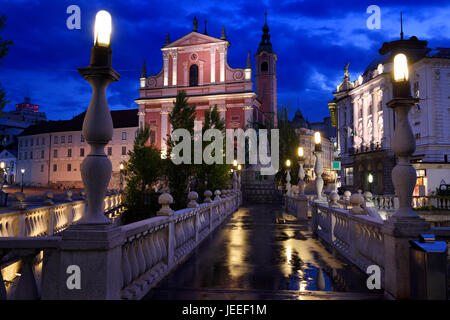 Reflexionen über nasse Triple Bridge nach Regen in der Dämmerung mit Lichtern auf Franziskanerkirche der Verkündigung und Central Apotheke Ljubljana Slowenien Stockfoto