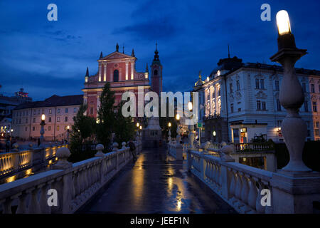 Reflexionen über nasse Triple Bridge nach Regen in der Dämmerung mit Lichtern auf Franziskanerkirche der Verkündigung und Central Apotheke Ljubljana Slowenien Stockfoto