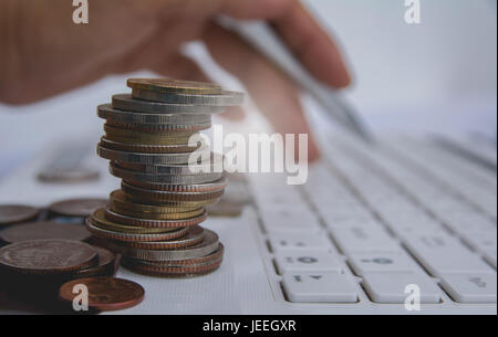 Stapel Münzen auf weißer Laptop und Finger drücken Sie die Taste auf der Tastatur. Finanzielle und speichern. Stockfoto