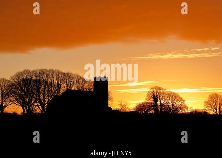 St. Margarets Kirche Burnham Norton mit einem Post Sonnenuntergang glühenden Himmel und Bäume Silhouette Stockfoto