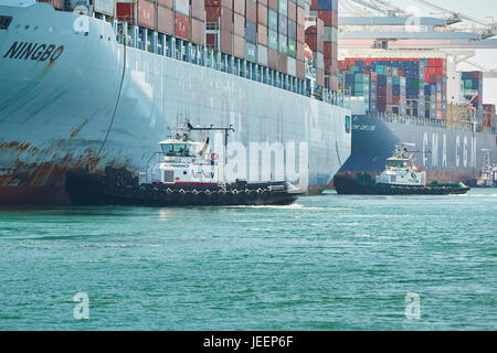 Das riesige COSCO Ningbo Containerschiff orientiert sich in Liegeplatz J270 am Pier J an zwei Traktor Schlepper am Containerterminal Long Beach, Los Angeles, USA. Stockfoto