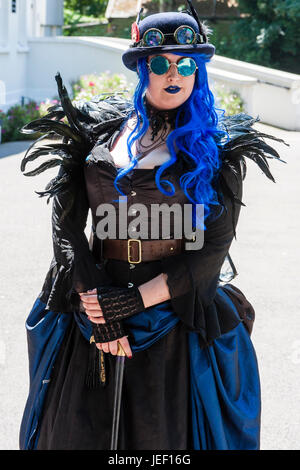 Steampunk kaukasische Frau, 20 Jahre, groß bauen, stehend im Sonnenschein mit schwarzen Kostüm und Hut mit Schutzbrillen, lange blaue Haare. Stockfoto