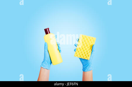 Weibliche Hände in Gummihandschuhe halten Waschmittel in einer Flasche und einem Schwamm auf blauem Hintergrund Stockfoto