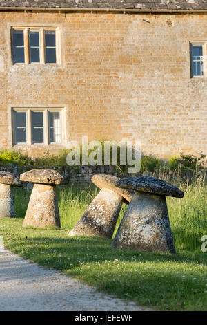 Staddle Steinen vor einem Haus in dem Dorf Wyck Rissington in den späten Abend Juni Sonnenschein. Cotswolds, Gloucestershire, England Stockfoto