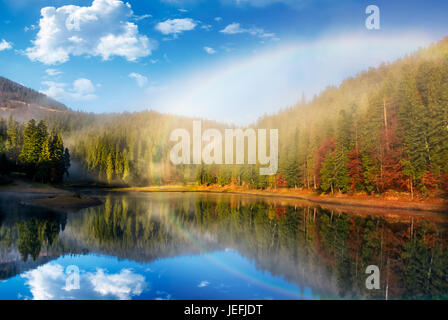 Regenbogen über dem malerischen See im nebligen Fichtenwald. majestätische Herbst Sonnenaufgang in wunderschöne Landschaft mit schönen Wetter Stockfoto