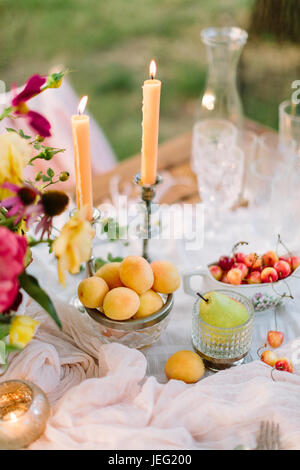 Picknick, Partnersuche, Hochzeit, Valentinstag, Wochenenden Konzept - romantischen Tisch für Brautpaar mit Blumen, brennende Kerzen, Kristallgläser und solche behandeln wie Aprikosen, Birnen und Kirschen Stockfoto