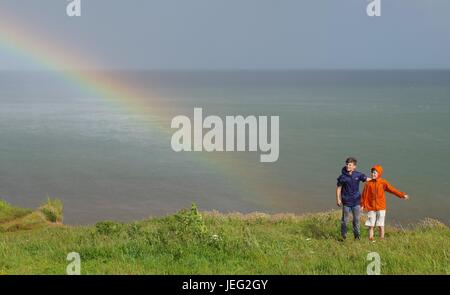 Zwei Jungs auf Langstone Felsen mit einem Regenbogen über dem Ärmelkanal. Dawlish, Devon, UK. Juni 2017. Stockfoto