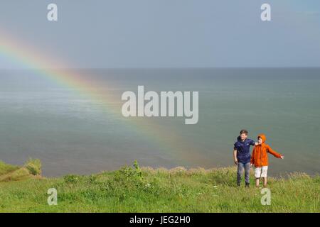 Zwei Jungs auf Langstone Felsen mit einem Regenbogen über dem Ärmelkanal. Dawlish, Devon, UK. Juni 2017. Stockfoto