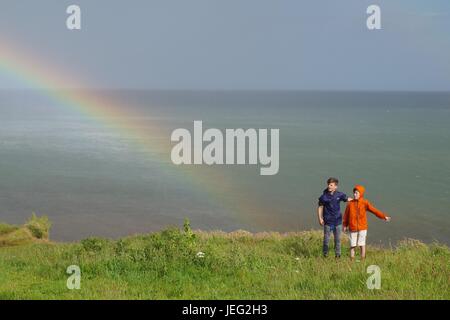 Zwei Jungs auf Langstone Felsen mit einem Regenbogen über dem Ärmelkanal. Dawlish, Devon, UK. Juni 2017. Stockfoto