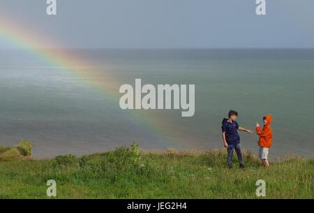 Zwei Jungs auf Langstone Felsen mit einem Regenbogen über dem Ärmelkanal. Dawlish, Devon, UK. Juni 2017. Stockfoto