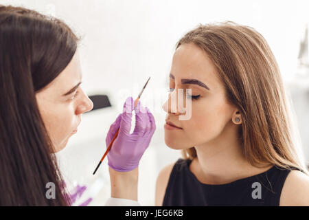 Porträt von professionellen Kosmetikerin in lila Handschuhe machen permanente Augenbrauen Stockfoto