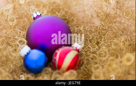 Eine Gruppe mit drei Weihnachtskugeln, einem großen lila mit satinierte Oberfläche, einem kleinen blauen und eine kleine rot und Gold auf gold-glitter Stockfoto
