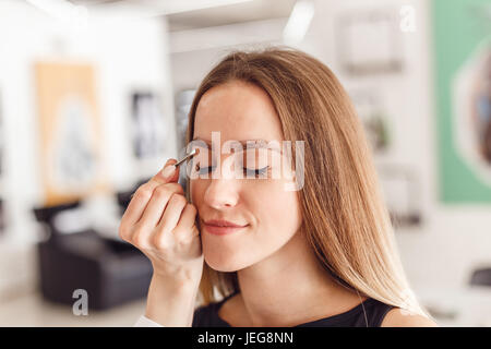 Junge Frau tweezing ihre Augenbrauen im Schönheitssalon. Stockfoto