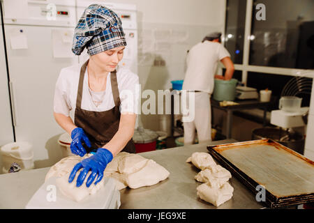 weibliche Bäcker Hände abschneiden Stück Teig mit alten Teig Scrapper Messer über Metall Bäckerei Tischfläche Stockfoto