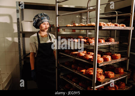 Baker steht in der Nähe von Regalen mit frischen Brötchen Stockfoto