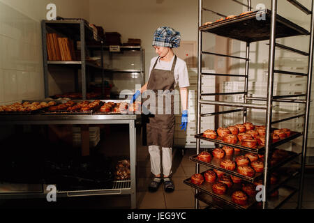 Baker steht in der Nähe von Regalen mit frischen Brötchen Stockfoto