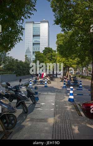 Elektro-Scooter auf Bürgersteig geparkt und Gegenlicht durch Sonne reflektiert Bürohaus, Suzhou Industrial Park, Suzhou, Jiangsu, China Stockfoto