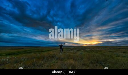 Mann, stehend mit seinen Armen verteilt offen bei Tagesanbruch im Grasslands National Park; Saskatchewan, Kanada Stockfoto