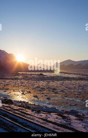 Gleise liegen im Vordergrund als Sonnenaufgang Gipfeln über Chugach Berge Aufleuchten einer eisigen Turnagain Arm; Alaska, Vereinigte Staaten von Amerika Stockfoto