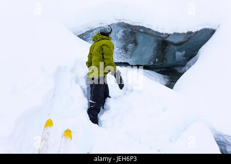 Ein Mann beobachtet einen Stream ausgehend unter Fels-Gletscher in Alaska Range im Januar; Alaska, Vereinigte Staaten von Amerika Stockfoto
