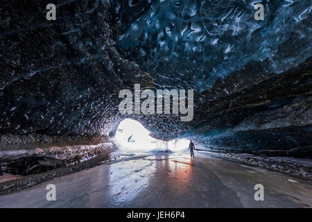 Ein Mann steht in der Nähe der Einfahrt in einen Tunnel unter dem Eis des Gletschers Canwell mit den Farben des Sonnenuntergangs reflektiert das Eis im winter Stockfoto