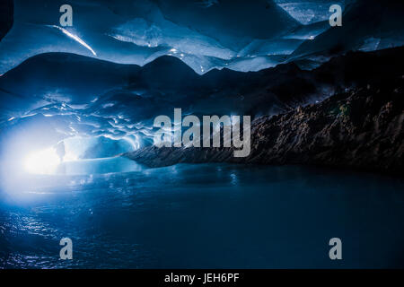 Ein Mann ist am Eingang zu einer dunklen Eishöhle innerhalb Augustana-Gletscher in Alaska Range Silhouette; Alaska, Vereinigte Staaten von Amerika Stockfoto