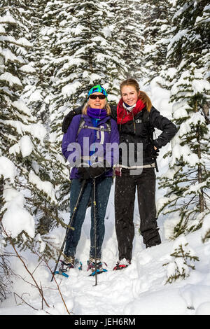 Zwei weibliche Schneeschuhwanderer auf einer Schnee bedeckten Rundweg um verschneite immergrünen Bäumen; Kananaskis Country, Alberta, Kanada Stockfoto
