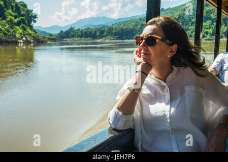 Eine Frau mit Sonnenbrille sitzt in einem Ausflugsboot, schaut aus dem Fenster dabei auf dem Mekong Fluss; Der Provinz Luang Prabang, Laos Stockfoto