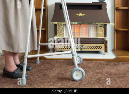 Ältere Dame in ihrem Zimmer Frame stehen in der Nähe von Gas der neunziger Feuer. Stockfoto