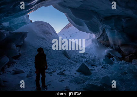 Im Winter steht ein Silhouette Mann hinter dem Eingang eine Eishöhle in Augustana Gletscher in die Alaska Range. Stockfoto