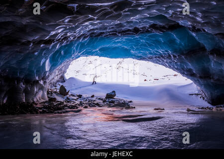 Ein Mann wird umrahmt von den Eingang zu einer großen Eishöhle in der Nähe der Endstation der Augustana-Gletscher in Alaska Range im winter Stockfoto