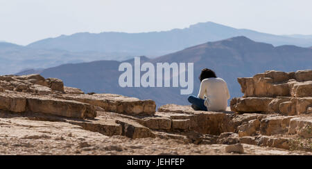 Eine Person sitzt auf einem Felsen mit Blick auf die schroffe Landschaft, Ramon Nature Reserve; Mitzpe Ramon, South District, Israel Stockfoto
