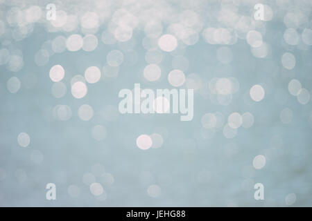 Verschwommene Wasseroberfläche mit Wellen glitzern in der Sonne. Sonnenlicht-Bokeh-Hintergrund Stockfoto