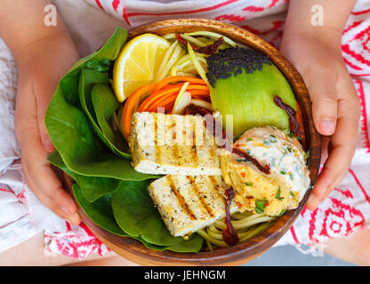 Buddha-Schüssel mit gegrilltem Tofu und Gemüse in die Hände des Kindes. Kind-Vegan-Konzept. Stockfoto