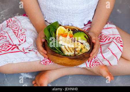 Buddha-Schüssel mit gegrilltem Tofu und Gemüse in die Hände des Kindes. Kind-Vegan-Konzept. Stockfoto