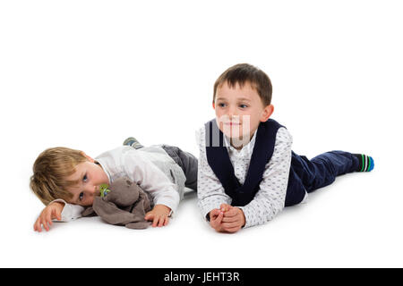 2 kleine Brüder tragen festliche Kleidung auf dem Boden, mit Plüsch Tier (Kaninchen) und Schnuller liegen. Isoliert auf weißem Hintergrund Stockfoto