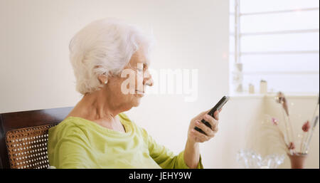 Glückliche alte Frau mit Smartphone, durch Berühren des Bildschirms und das Telefon zu Hause zu spielen. Stockfoto