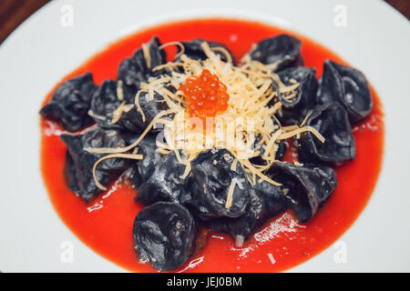 Schwarze Ravioli mit Lachs in Tomatensoße mit Käse und rotem Kaviar dekoriert. Stockfoto