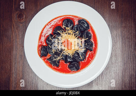 Schwarze Ravioli mit Lachs in Tomatensoße mit Käse und rotem Kaviar dekoriert. Stockfoto