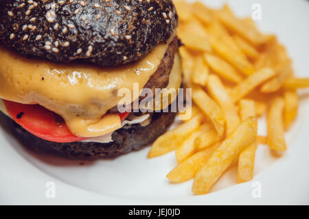 Schwarz-Burger auf weißen Teller mit Pommes frites serviert. Stockfoto