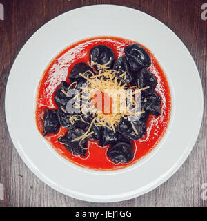 Schwarze Ravioli mit Lachs in Tomatensoße mit Käse und rotem Kaviar dekoriert. Stockfoto