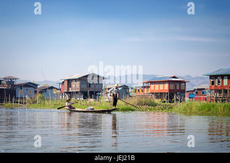 Häuser auf Holzpfählen und Burmesen in einem Boot in einem Dorf am Inle-See, Burma, Myanmar Stockfoto