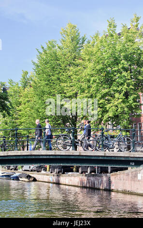 AMSTERDAM, 27. AUGUST 2014. Fußgänger auf einer Brücke mit geparkten Fahrrädern. Amsterdam ist international bekannt als Venedig des Nordens. Stockfoto