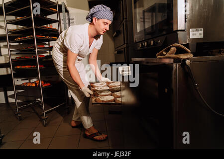 Einnahme von frisch gebackenem Brot aus dem Ofen in einer modernen Bäckerei Bäcker Stockfoto