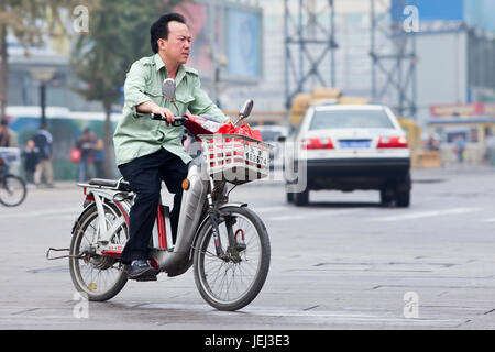 PEKING – ÜLG. 12, 2011. Mann auf dem Elektrofahrrad in Peking. Derzeit kaufen viele Einwohner Pekings batteriebetriebene Fahrräder, um Staus zu vermeiden. Stockfoto